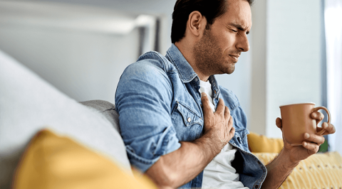 Man sitting with a cup hold chest in pain